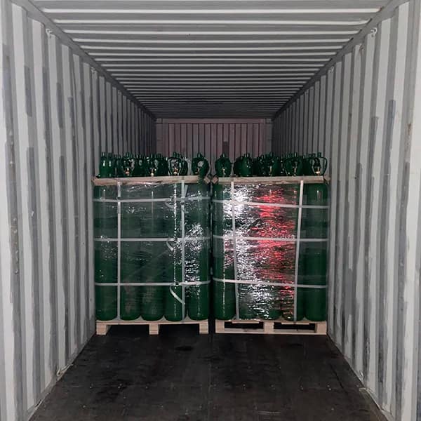 Row of high‑pressure gas cylinders standing upright on a metal pallet, valve guards installed, wrapped and labeled for outbound shipping